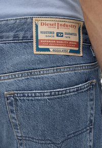 Οπίσθια όψη μπλε τζιν από denim που δείχνει μια ετικέτα Diesel Industry με κείμενο για ποιοτικά τζιν και καταχώριση από το 1978.