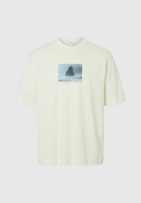 Krämfärgad t-shirt med kort ärm i bomull, med en rektangulär grafisk tryck av en stenig landskap med havsvågor.