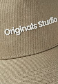 Casquette de baseball kaki avec une texture de tissu lisse, présentant "Originals Studio" en lettres blanches en gras sur le devant.