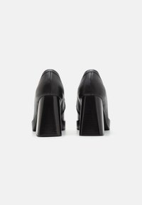 Black leather heels with a chunky, square-shaped heel. Smooth texture, minimalist design, and visible stitching detail at the seam.