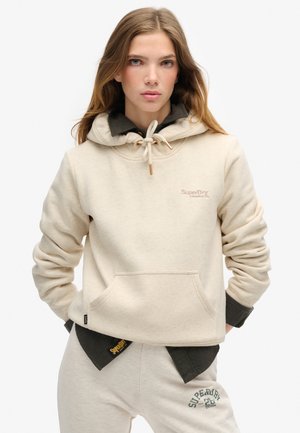 Sweatshirt à capuche crème avec poche avant, fermeture à cordon de serrage et logo brodé. Associé à un pantalon de survêtement beige avec un logo vert.