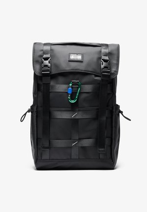 Juodas nailono kuprinė su sukama viršuje, turinti reguliuojamas diržus, priekinį logotipą ir pritvirtintą žalią karabinerį. Minimalistiniai akcentai.