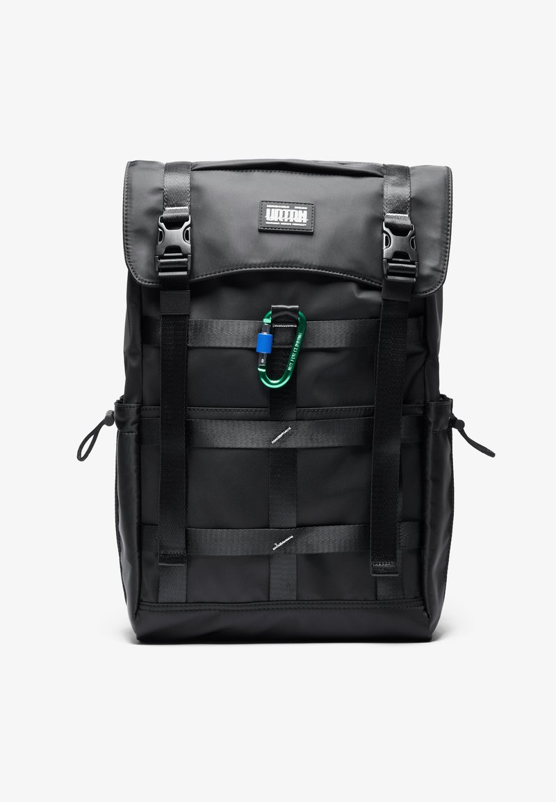 Musta nailonireppu, jossa on käännettävä yläosa, säädettävät hihnat, etuosa logolla ja vihreä karabiini kiinnitettynä. Minimalistiset yksityiskohdat.