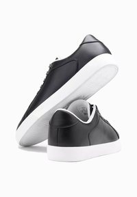 Czarne skórzane sneakersy o gładkiej powierzchni, z białą gumową podeszwą i szarymi sznurowadłami. Posiadają niski krój z kontrastowymi wykończeniami.