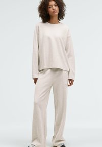 Beige cotton-blend loungewear set featuring a loose-fit, long-sleeve top with a round neck and wide-leg pants, both with subtle stitched detailing.