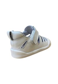 Sandalia blanca para niño pequeño con correa de Velcro y costados recortados, hecha de cuero suave y suela de goma, vista en ángulo que muestra el talón y el lado.