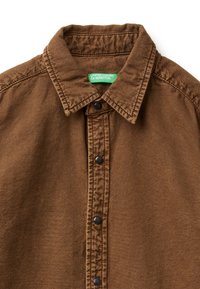 Brązowa koszula na guziki wykonana z tkaniny o fakturze, z klasycznym kołnierzem, czarnymi zatrzaskami i zieloną metką wewnątrz.