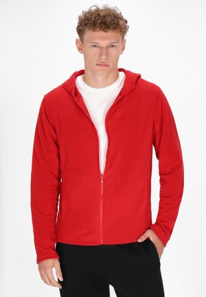 Rode fleece hoodie met rits aan de voorkant, lange mouwen en een capuchon, gedragen over een wit shirt. Gladste structuur en casual pasvorm.