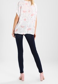 Blouse à manches courtes à motif floral en blanc doux avec des accents roses, associée à un jean skinny foncé et des chaussures à talons roses clairs.