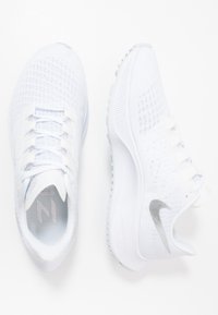 Scarpe sportive bianche realizzate in tessuto a rete leggero, con un motivo testurizzato, collare imbottito e un logo swoosh argentato di lato.