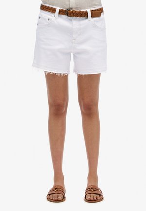 Shorts en denim blanc avec un ourlet effiloché, dotés de passants de ceinture. Associés à une ceinture tressée marron et des sandales à glisser marron sur des pieds nus.