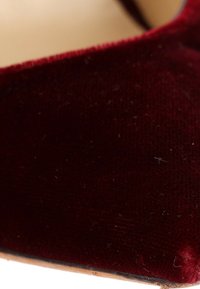 Gros plan d'un tissu en velours rouge foncé avec une surface texturée et de petites fibres peluches visibles.