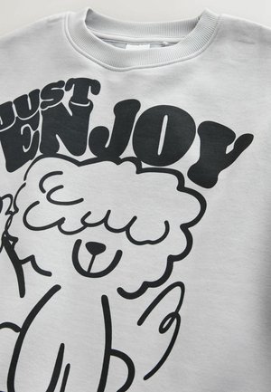 Sivá mikina s čiernym grafickým motívom kresleného ovce a textom "JUST ENJOY" v tučnom, hravom písme.