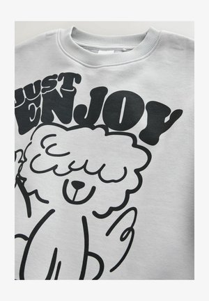Gray sweatshirt featuring a black graphic design of a cartoon sheep with the text "JUST ENJOY" in bold, playful font.
