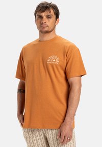 Pánské oranžové tričko z bavlny s krátkými rukávy, na levé straně hrudi s bílým logem slunce a nápisem "Quiksilver". Měkká, hladká textura.