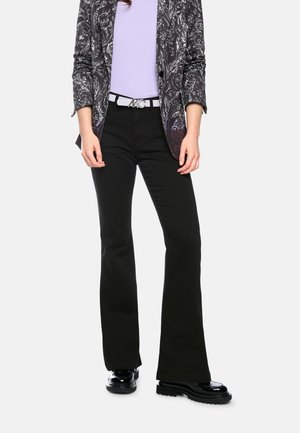 Woman wearing black patterned blazer, light purple top, black flared pants, white belt with silver buckle, and black shiny shoes.