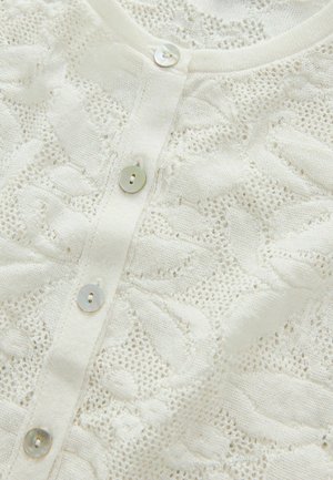 White knitted cardigan featuring a textured, openwork design and four pearl-like buttons down the front. Soft, delicate fabric.
