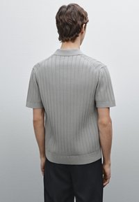 Grey knitted polo shirt with short sleeves, featuring vertical ribbed texture and a straight hem. Worn with black trousers.