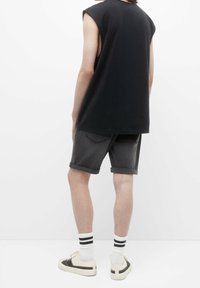 Top negro sin mangas, pantalones cortos de mezclilla gris con dobladillos enrollados, calcetines blancos con rayas negras y zapatillas beige; diseño minimalista.