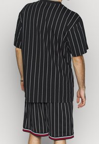 Czarny, oversize-owy t-shirt w paski z krótkimi rękawami, zestawiony z czarnymi szortami z czerwono-białymi paskami na krawędzi.