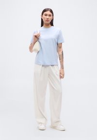 Γαλάζιο βαμβακερό μπλουζάκι με στρογγυλή λαιμόκοψη, με λευκό κείμενο "Calvin Klein Jeans". Συνδυασμένο με άνετο λευκό παντελόνι και μικρή κρεμ τσάντα.