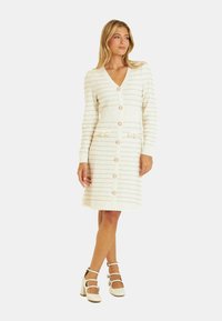 Abito bianco lavorato a maglia con scollo a V, maniche lunghe e chiusura con bottoni; presenta righe testurizzate, vita a costine e dettagli decorativi a forma di fiore.