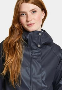 Marinblå vattentät jacka med hög krage, slät textur och tryckknappsdetaljer, med en modern passform och avslappnad design.