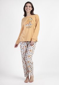 Conjunto de pijama de dos piezas. Parte superior de manga larga en mostaza con gráfico de perro de dibujos animados y texto. Pantalones crema estampados con diversas ilustraciones de animales.