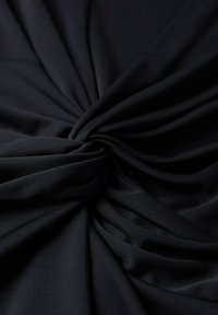 Tissu noir noué en un nœud central, révélant des plis doux et une texture avec des contrastes subtils de lumière et d'ombre.