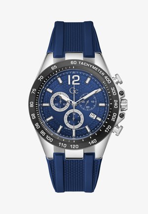 Zegarek chronograf z niebieską teksturowaną tarczą, srebrnymi akcentami, czarną bezelą tachymetryczną i niebieskim paskiem gumowym z wzorem w strukturę plastra miodu.