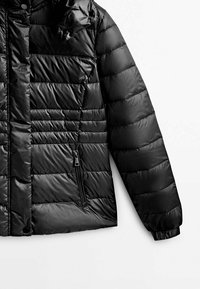 Sort puffjakke med en quiltet design, lynlås-lomme foran, elastiske manchetter og hætte. Fremstillet af blankt, vandtæt materiale.