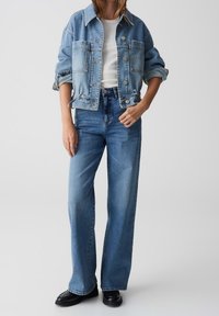 Světle modrá denimová bunda s volným střihem, dvěma předními kapsami, spojená s vysokými světle modrými džíny a černými kotníkovými botami.