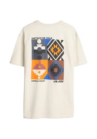 T-shirt en coton beige avec un imprimé graphique comprenant des formes géométriques colorées et le texte "Santiago de Chile" et "Pics Andins".
