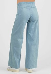 Light blue wide-leg pants made of a soft, lightweight fabric. Elastic waistband, minimal stitching detail, and worn with white sneakers.