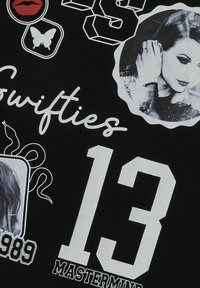 Čierna tkanina s bielymi a červenými grafickými potlačami, vrátane čísla "13," "Swifties," a obrázkov motýľa a pier.