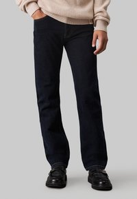 Jeans en denim bleu foncé avec une coupe droite et un design classique à cinq poches, présentant des coutures subtiles et une légère texture usée.
