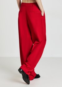 Pantalons rouges au design fluide, avec une taille haute, des poches latérales et une texture lisse ; associés à des chaussures noires.