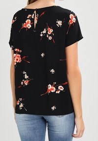 Camiseta negra de manga corta con un estampado floral en rojo y blanco, con un detalle de ojal en la parte posterior del escote y una textura de tela suave.