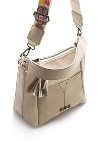 Borsa a tracolla in pelle beige con apertura con cerniera, tracolla regolabile in tessuto intrecciato con motivi colorati e nappe decorative sul davanti.
