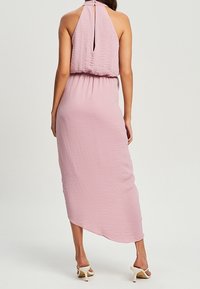Rosa, ärmelloses Maxikleid aus strukturiertem Stoff, mit Halsband und offenem Rücken. Es zeigt eine elastische Taille und einen asymmetrischen Saum.