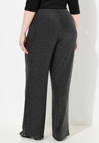 Pantalons noirs à large jambe avec une texture scintillante, dotés d'une taille élastique et d'une finition lisse, présentés de dos.