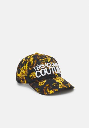 Gorra de béisbol negra con patrón barroco amarillo y gran texto blanco bordado "Versace Jeans Couture" en la parte delantera.