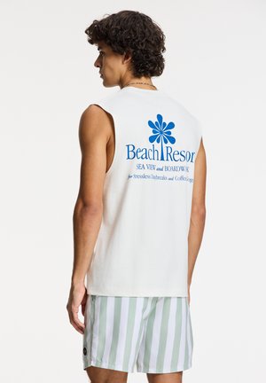 Sleeveless cream tank top with blue graphic "Beach Resort" text on the back. Paired with light green and white striped swim shorts.