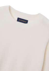 Crème-kleurige trui gemaakt van zachte stof, met een ronde hals, geribbelde manchetten en een label dat "PIOMBO" in blauw en goud leest.