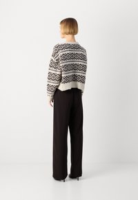 Maglione a maglia con un motivo geometrico in bianco e nero, design accorciato e orlo a coste, abbinato a pantaloni neri larghi e scarpe con tacco.