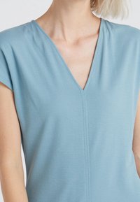 Top azzurro chiaro a maniche corte con scollo a V, texture morbida e dettaglio di cucitura verticale al centro. Adatto per un look casual.