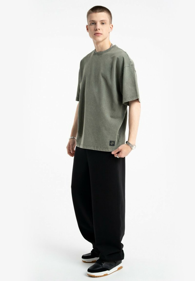 Zielona, oversize bawełniana koszulka z okrągłym dekoltem, podwiniętymi rękawami i małą naszywką z logo; w połączeniu z czarnymi spodniami o szerokich nogawkach i trampkami.