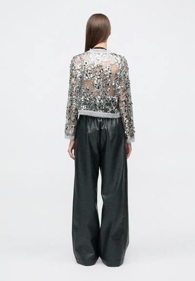 Διάφανη σακάκι με παγιέτες και ασημένιες διακοσμήσεις, εφαρμοστό στη μέση με ριμπ τελείωμα, συνδυασμένο με μαύρο δερμάτινο παντελόνι φαρδιάς γραμμής.