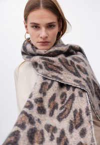 Leopardprint tørklæde i blød uldblanding, med nuancer af grå og varm brun, samt uferdige kanter langs kanten.