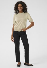 Beež lühikeste varrukatega kampsun siledat tekstuuri, mustade sirgete pükstega ja mustade tasaste kingadega, luues vabaaja rõivastuse.